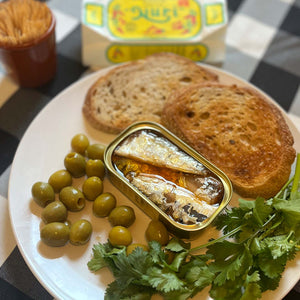 Nuri Extra Spiced Sardines in Olive Oil in an opened can, served with bread and olives