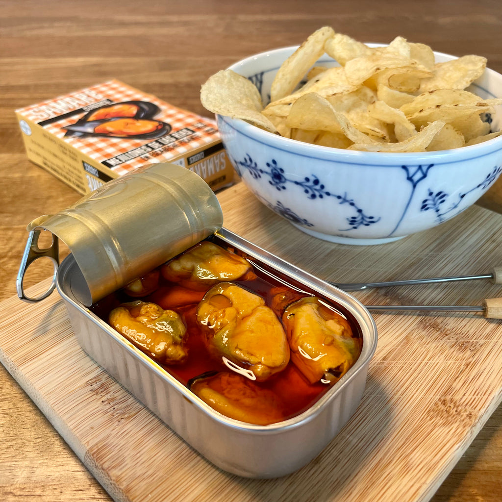 An opened tin of Samare Mejilliones en Escabeche Picante, served beside a bowl of potato chips