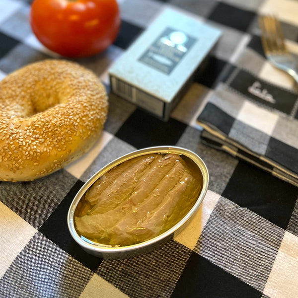 Ramón Peña Yellowfin Tuna Belly in Olive Oil served in an opened tin, beside a bagel